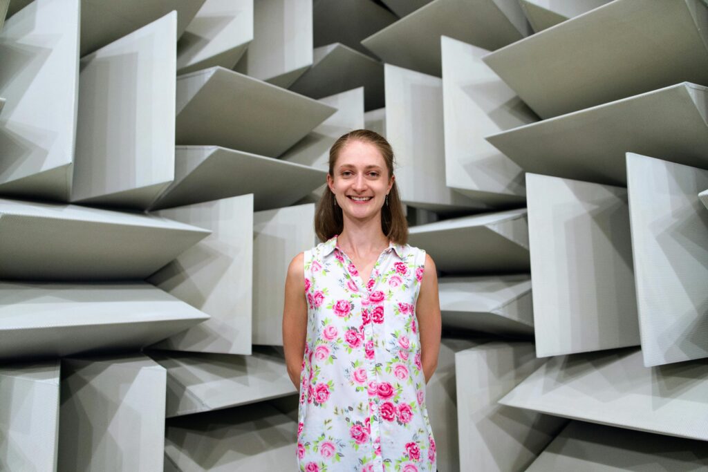 Smiling woman standing inside an acoustic engineering chamber with soundproof panels.